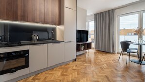 A modern kitchen with built-in appliances, a dining area with a table and chairs, and a large window with curtains. - Pure Rental Premium Inżynierska (Wrocław)
