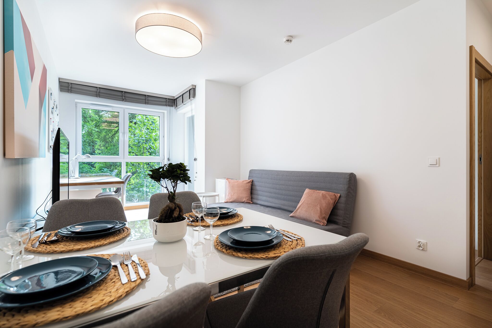 Un comedor moderno con una mesa de vidrio, sillas grises y un sofá gris.