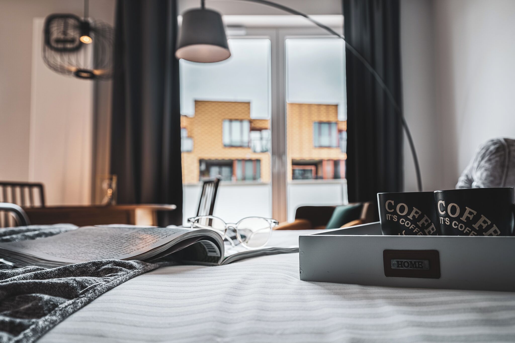 Ein ordentlich bezogenes Bett mit einem Laptop, einer Brille und Kaffeetassen auf einem Nachttisch.