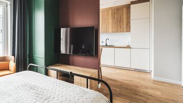 A modern hotel room with a bed, a desk, a television, and a kitchenette.