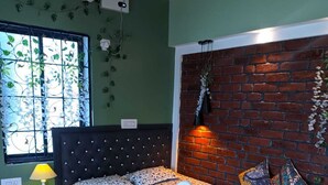 A bedroom with a bed featuring a swan design, a brick accent wall, a window with greenery, and a nightstand with a lamp. - Pravuprasad Homestay (Bhubaneshwar)