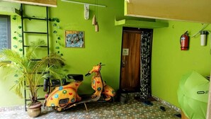 A room with a green wall, a wooden door, a scooter, a potted plant, and a fire extinguisher. - Pravuprasad Homestay (Bhubaneshwar)