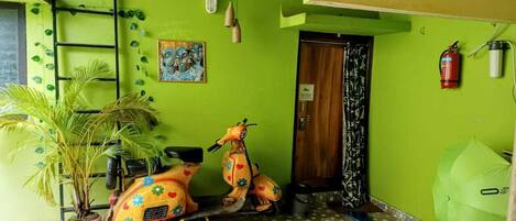A room with a green wall, a wooden door, a scooter, a potted plant, and a fire extinguisher.