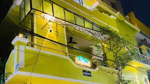 A multi-story building with a bright yellow facade, a gated entrance, and a parked scooter. - Pravuprasad Homestay (Bhubaneshwar)