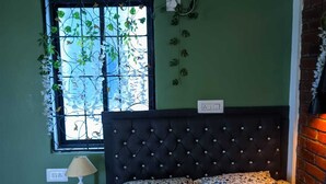 A bedroom with a bed, a window with plants, a wall-mounted air conditioner, and a brick wall. - Pravuprasad Homestay (Bhubaneshwar)