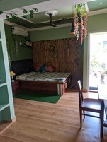 A bedroom with a bed, a chair, a wooden floor, a ceiling fan, and a window.
