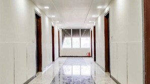 A long, narrow hallway with a shiny marble floor, white walls, and wooden doors on either side. - Hotel OPM & Restaurant (Agra)