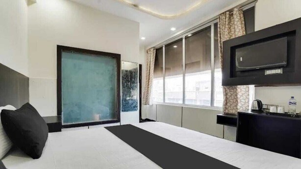 A hotel room with a large bed, a TV mounted on the wall, a window with curtains, and a small table with a kettle. - Hotel OPM & Restaurant (Agra)