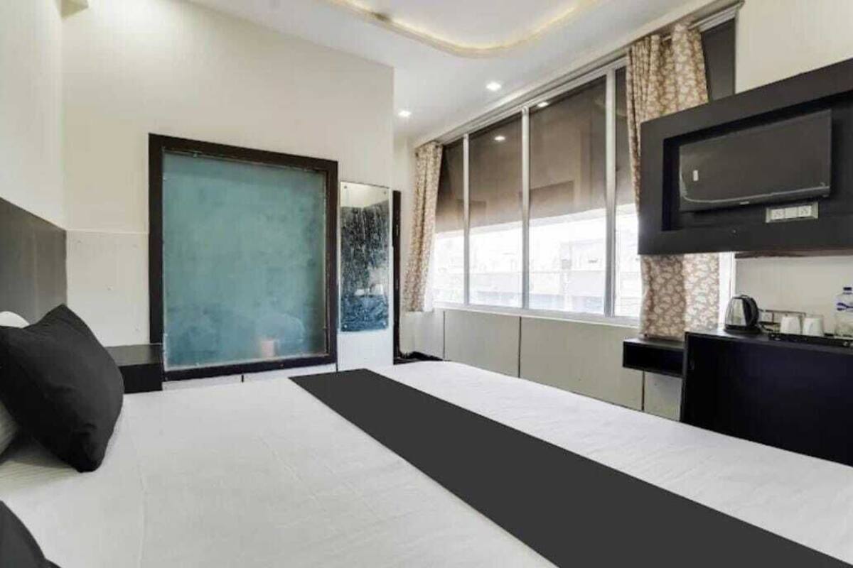 Habitación de hotel con una cama grande, un televisor montado en la pared, una ventana con cortinas y una mesita con un hervidor.