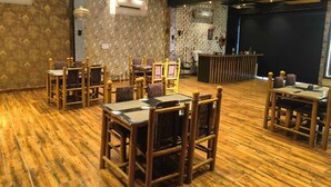 A restaurant with wooden flooring, patterned wallpaper, and multiple tables and chairs. - Hotel OPM & Restaurant (Agra)