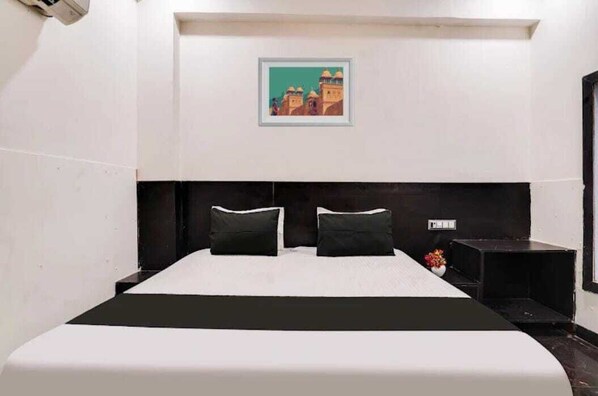 A hotel room with a large bed, a headboard, a small table with a vase, and a framed picture on the wall.