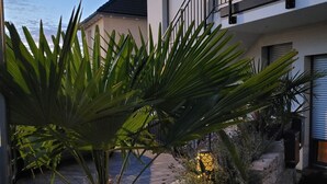 Um edifício moderno com varanda, um muro de pedra de contenção e um jardim com plantas e uma escultura decorativa de cogumelo.