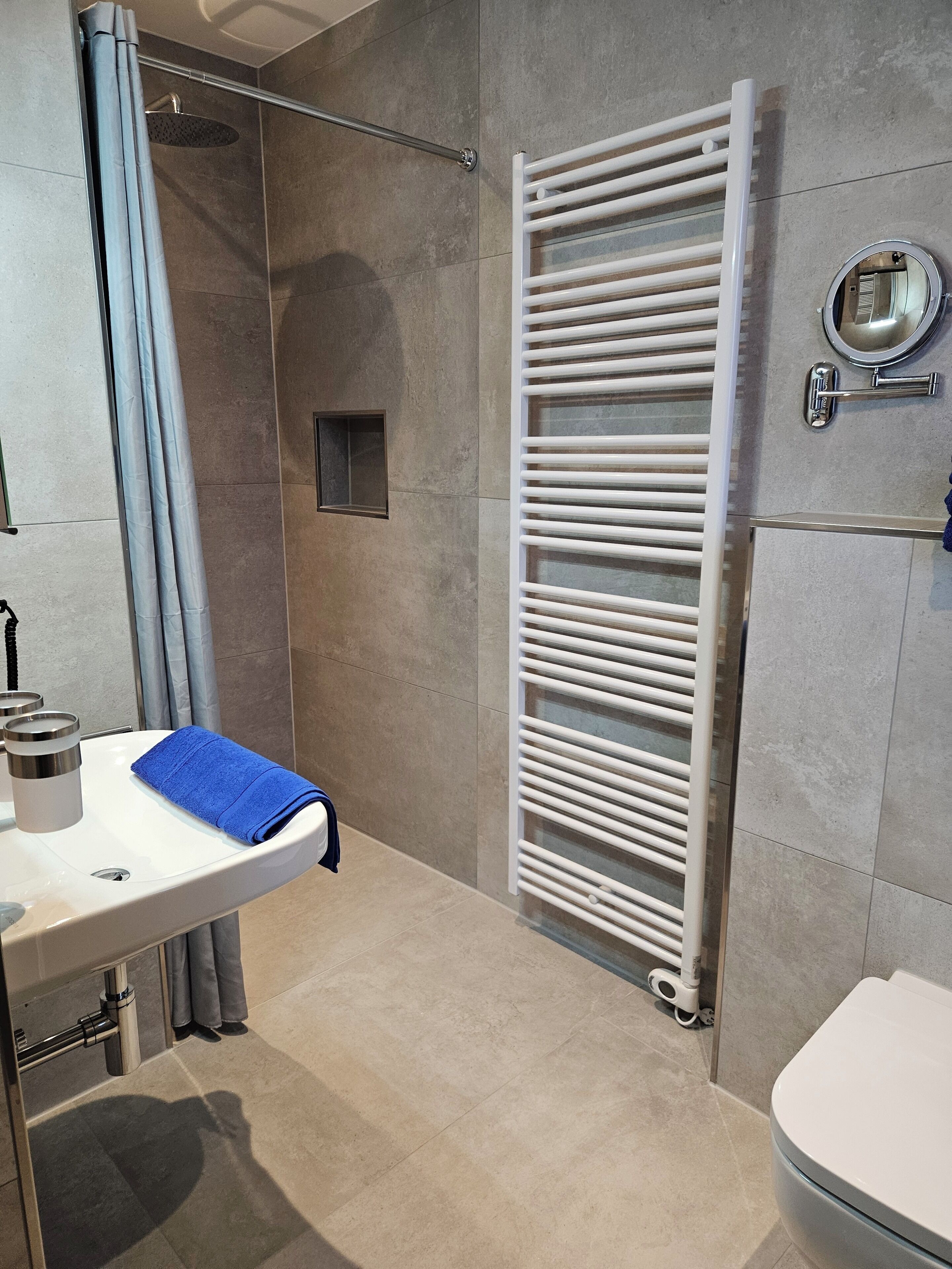 Un baño moderno con ducha, un lavamanos blanco y una toalla azul, además de un toallero blanco.