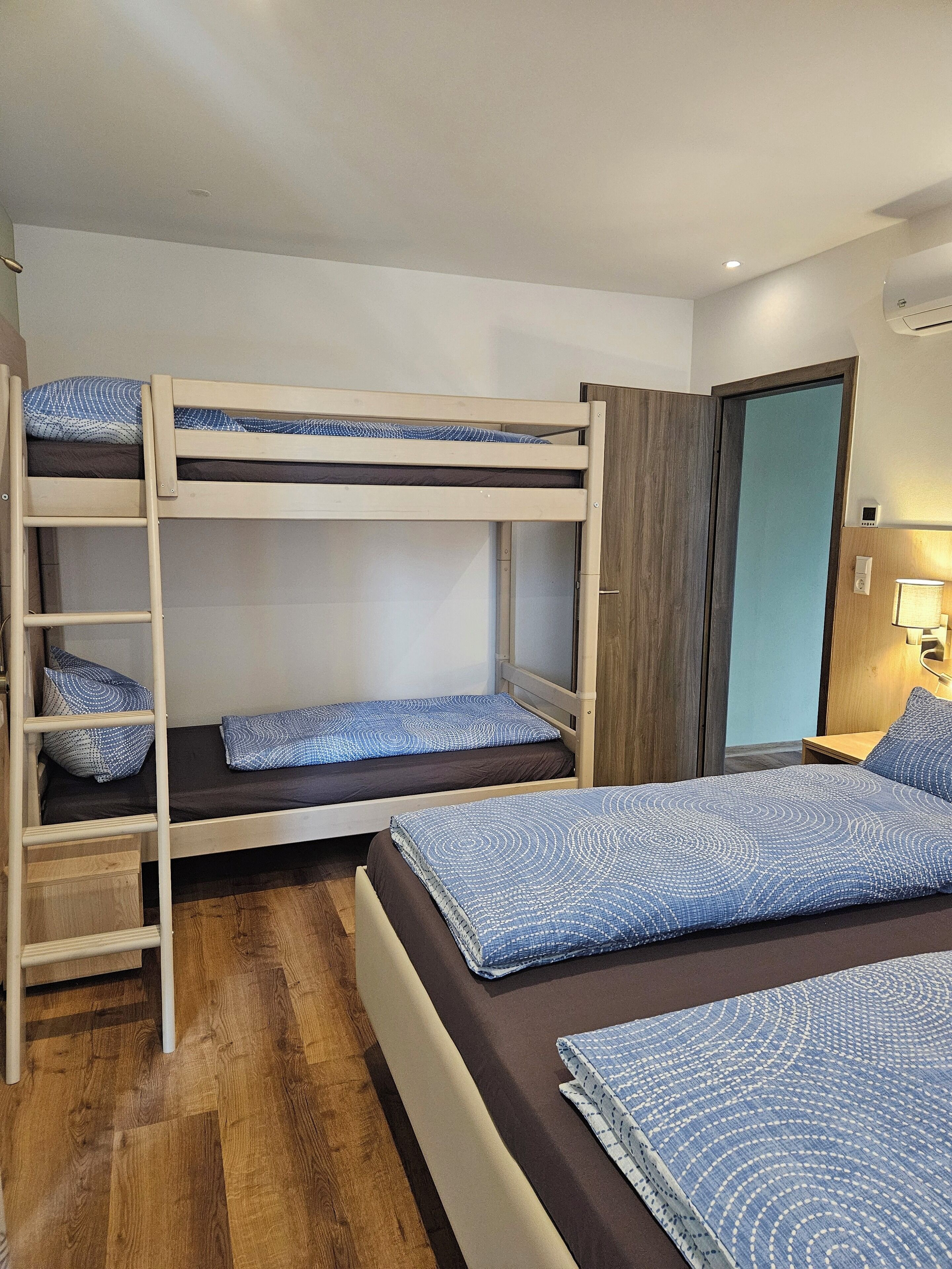 A bunk bed room with a wooden ladder, a wooden wardrobe, and a bedside table with a lamp.