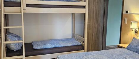 A bunk bed room with a wooden ladder, a wooden wardrobe, and a bedside table with a lamp.