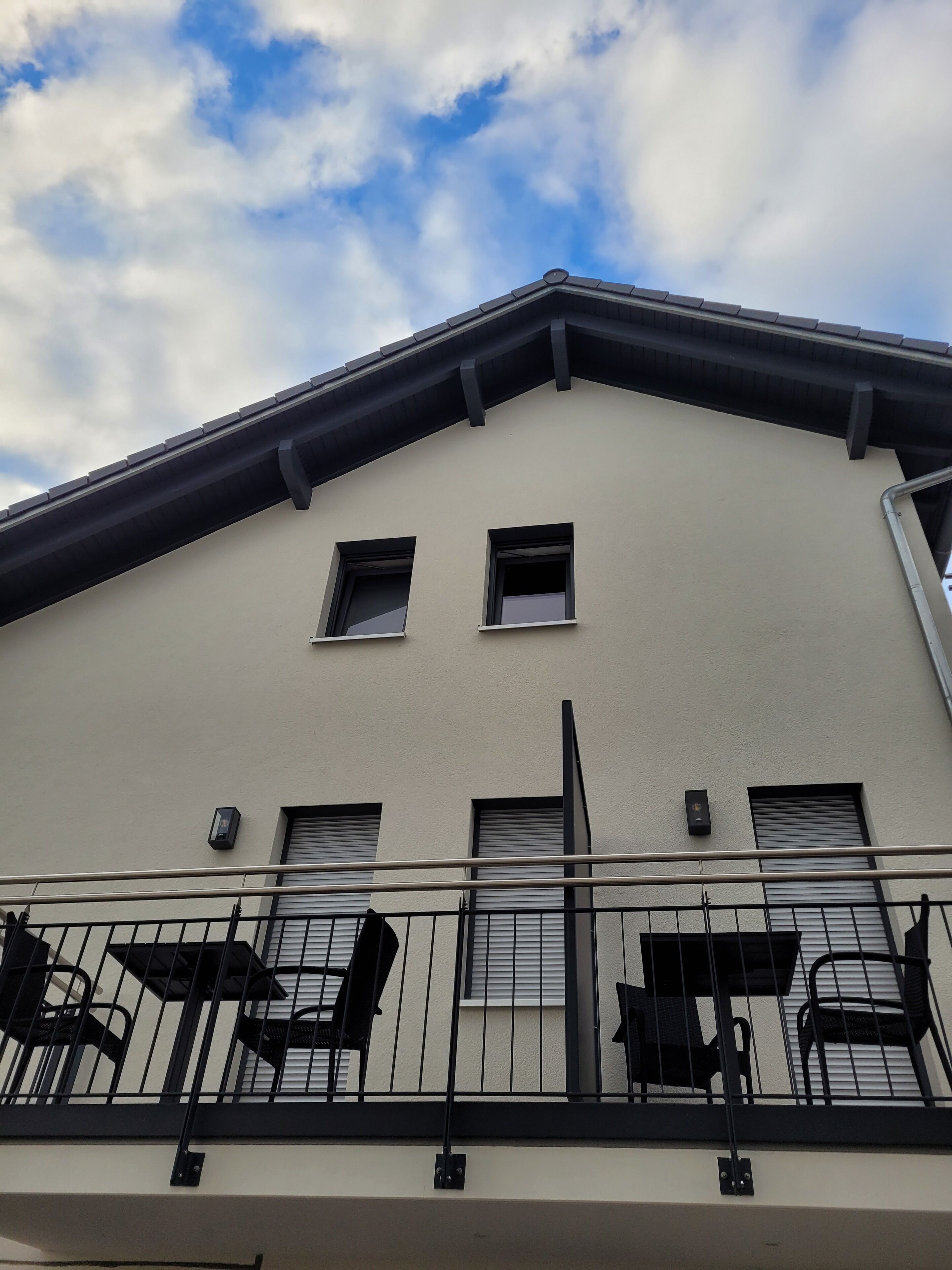A building with a flat roof, multiple windows, and a balcony with chairs.