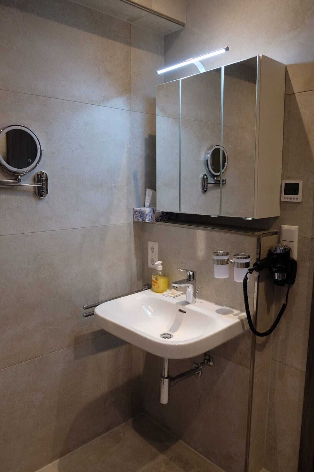 A modern bathroom with a white sink, a mirror, and a cabinet.
