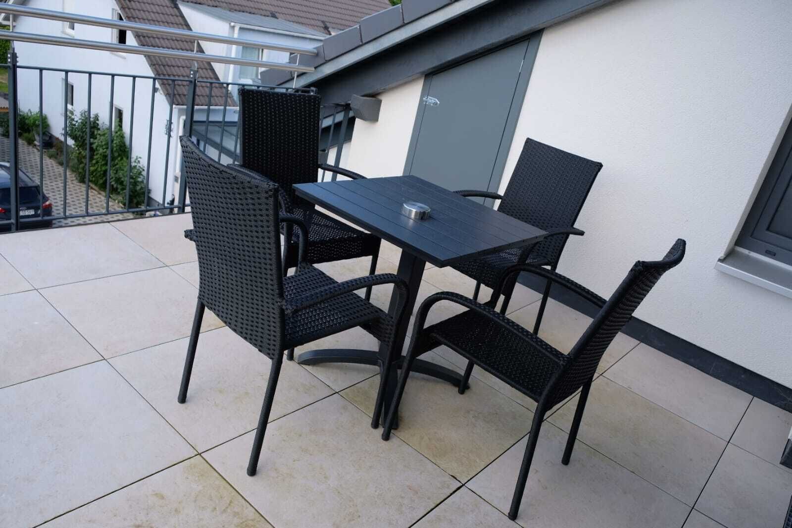 A balcony with a black table and four chairs, a metal railing, and a tiled floor.