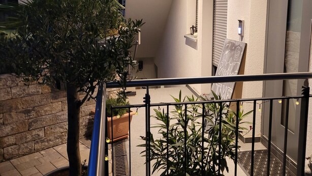 Varanda com vaso de planta, jardineira suspensa e placa indicando o endereço do edifício.
