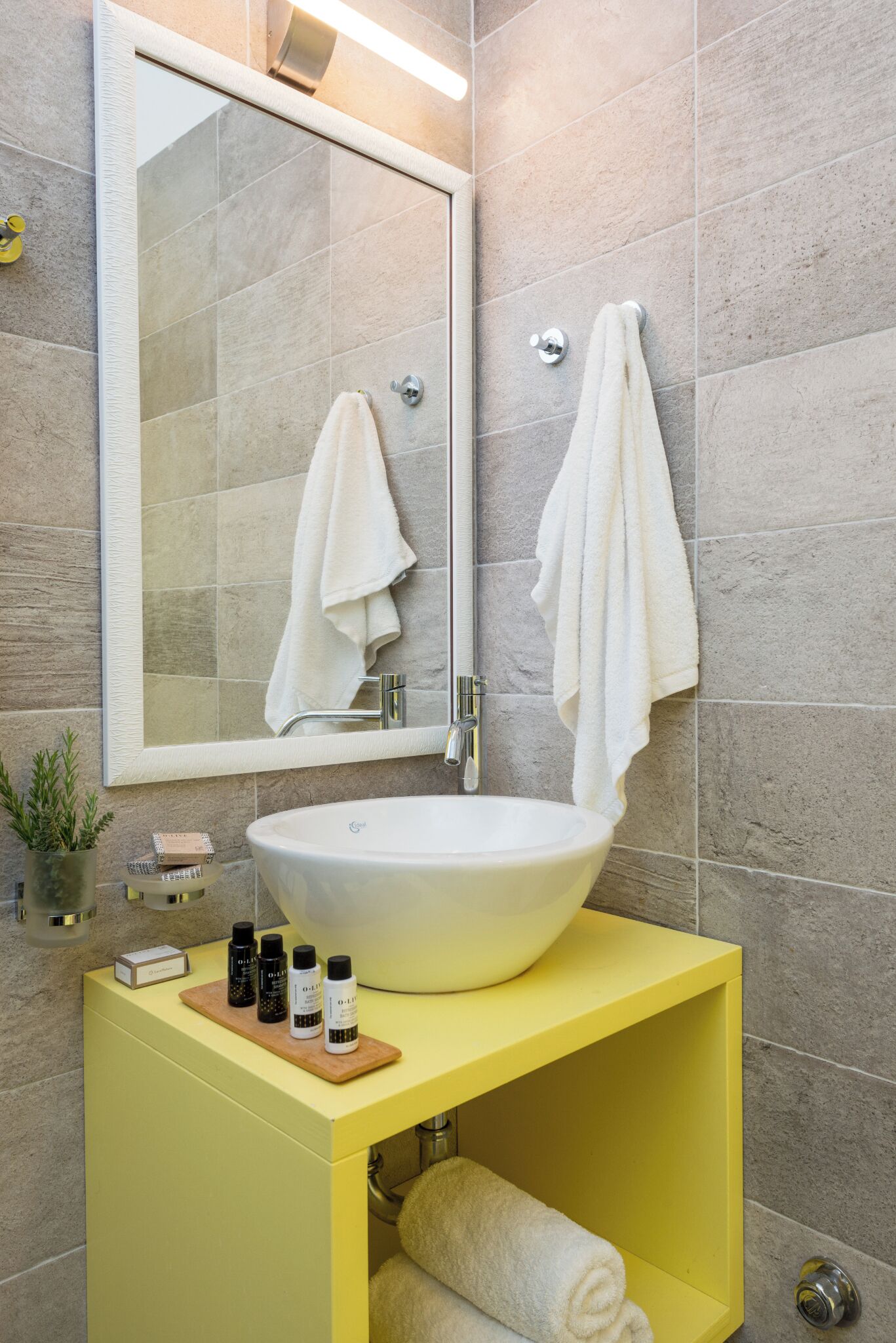 Un baño con un espejo grande, un lavamanos blanco y dos toallas colgadas en la pared.