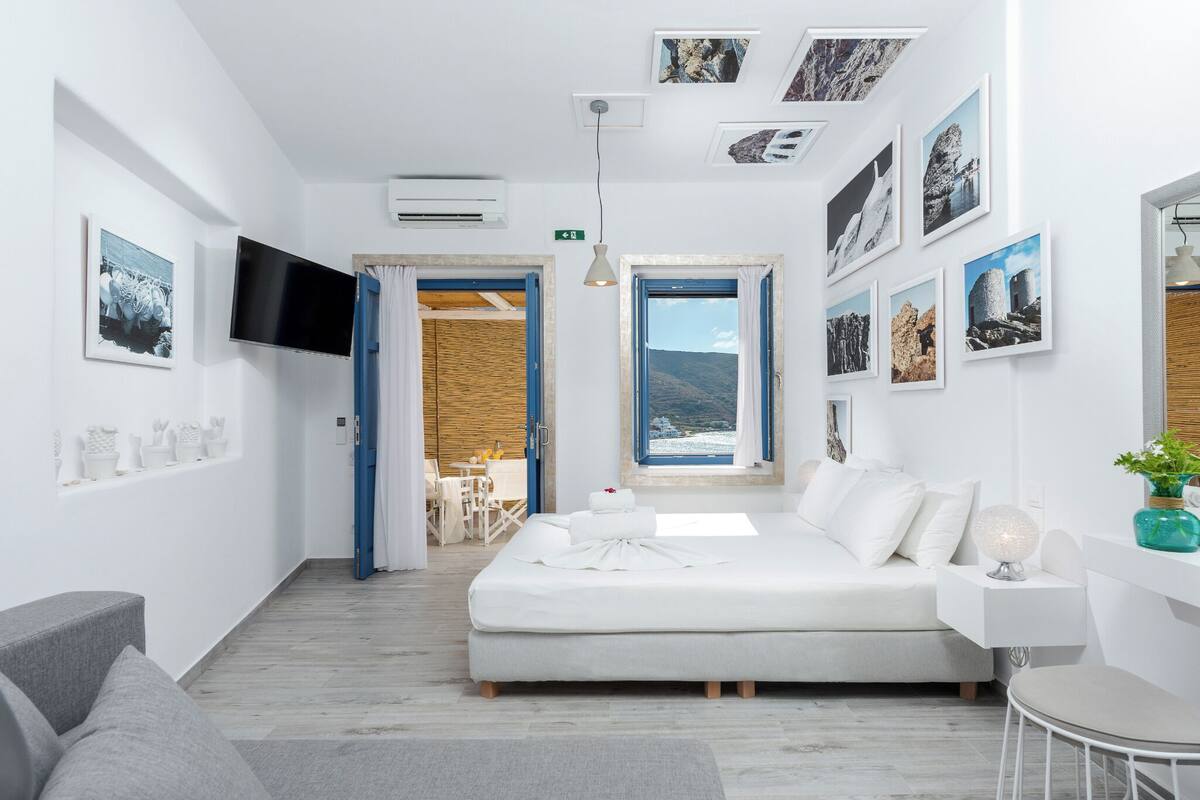 Moderni hotellihuone, jossa on sänky, televisio, ruokailutila ja taideteoksia seinillä.