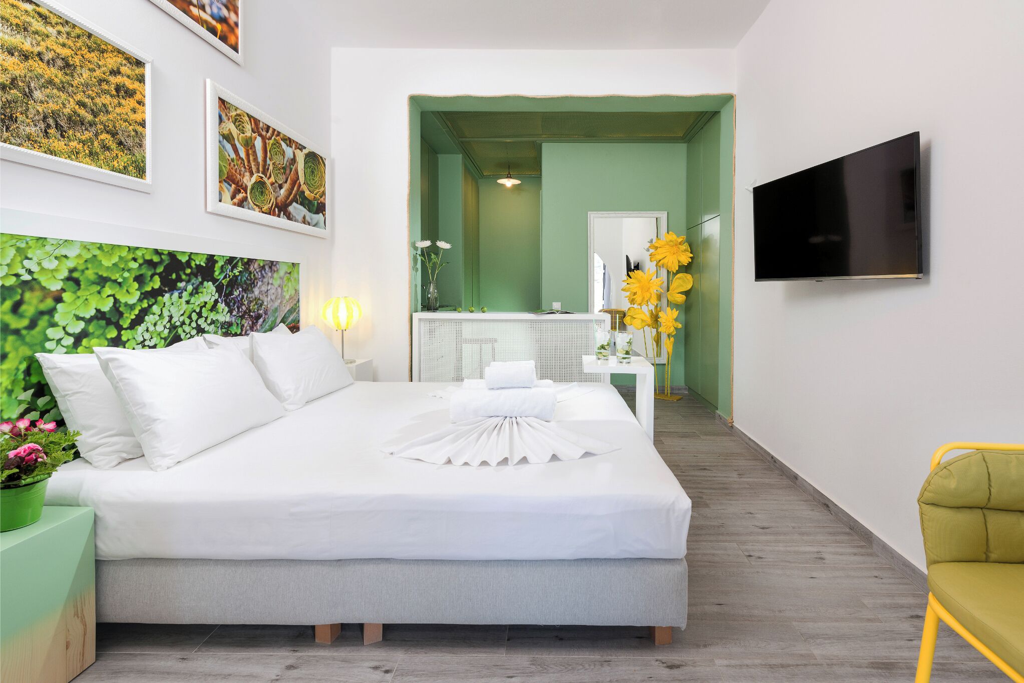 Ein Hotelzimmer mit Bett, Fernseher, grüner Wand und Kunstwerken.