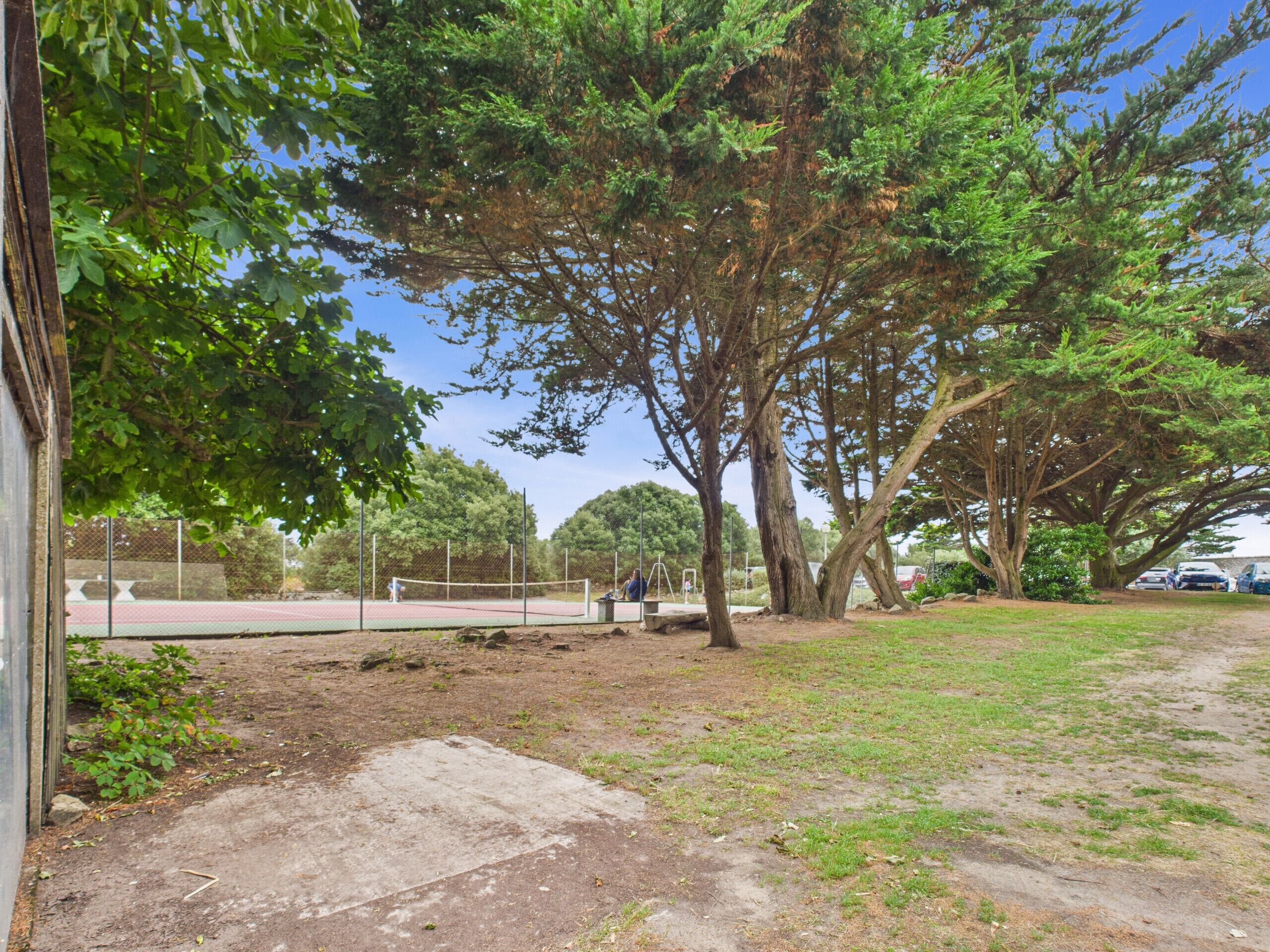 A tennis court with a net, surrounded by trees and a grassy area.