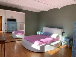 Een slaapkamer met een gebogen bed, een dressoir en een spiegel.