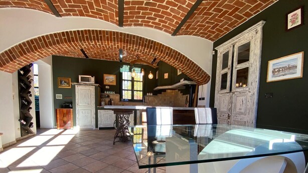 A spacious kitchen with a brick ceiling, a dining area with a glass table, and a view of the outdoors. - Charming Italian house in Cantarana for 6 guests, 3 bedrooms. (Piemonte)