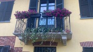 A building with a yellow facade, black shutters, and a balcony with purple flowers. - Charming Italian house in Cantarana for 6 guests, 3 bedrooms. (Piemonte)