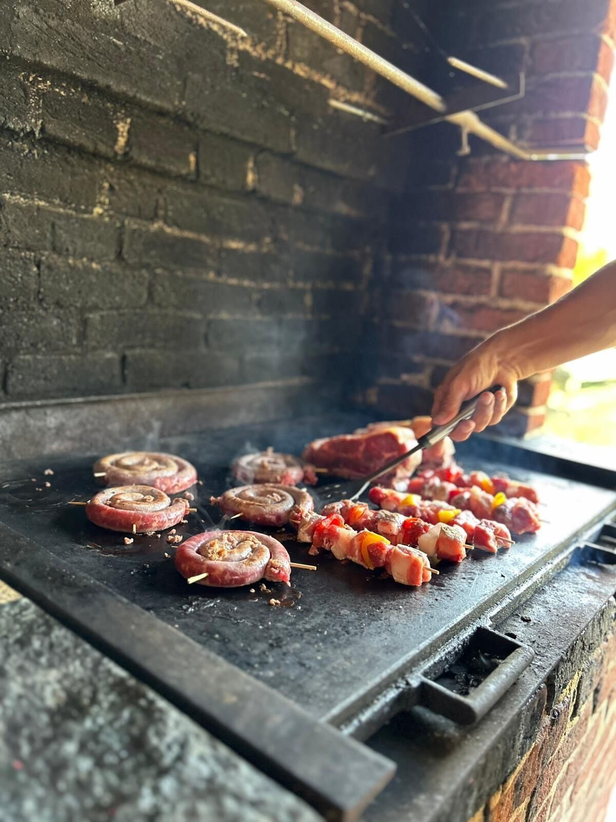 Une personne qui fait griller des saucisses et des brochettes sur un barbecue extérieur.