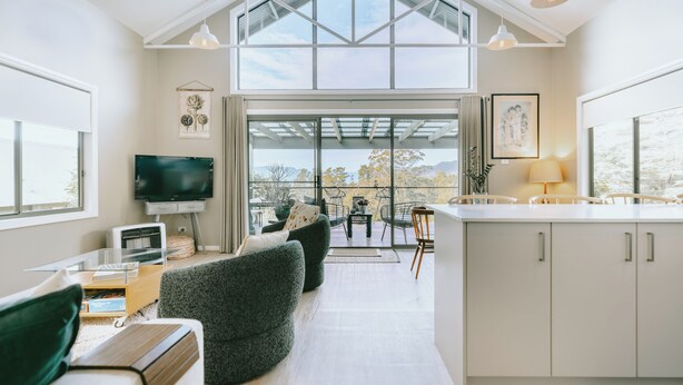A modern interior with a high ceiling, large windows, a dining area, and a kitchen. - Jimmy’s Cabin in Kangaroo Valey. Kangaroos, Kookaburras, sleeps 4! (Kangaroo Valley)