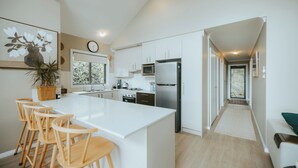 A modern kitchen with white cabinetry, a large island with bar stools, a microwave, a refrigerator, and a clock on the wall. - Jimmy’s Cabin in Kangaroo Valey. Kangaroos, Kookaburras, sleeps 4! (Kangaroo Valley)