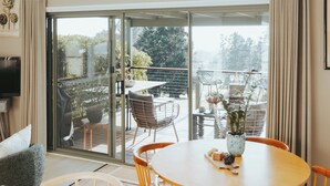 A spacious room with a large sliding glass door leading to an outdoor patio. There is a round wooden table with chairs, a ceiling fan, and a mounted TV. - Jimmy’s Cabin in Kangaroo Valey. Kangaroos, Kookaburras, sleeps 4! (Kangaroo Valley)