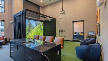 Quarto de hotel moderno com divisória de vidro, mesa de jantar, sofá e um pufe azul.