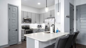 A modern kitchen with grey cabinets, stainless steel appliances, and a central island with bar stools.