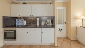 A compact kitchen with white cabinets, a built-in oven, a coffee maker, and a sink. - Vacation Rental: “Apartment on the Zingst Pier with a South-Facing Balcony” (Zingst)