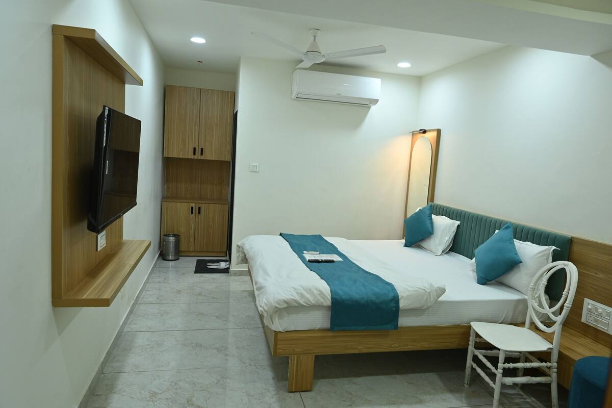 A bedroom with a bed, a TV mounted on the wall, a ceiling fan, and an air conditioning unit.