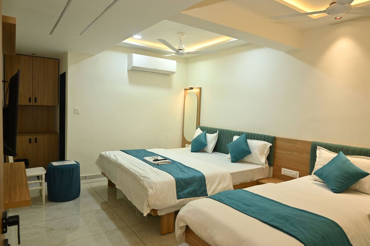 A hotel room with two beds, a ceiling fan, an air conditioning unit, and a small table with a chair.