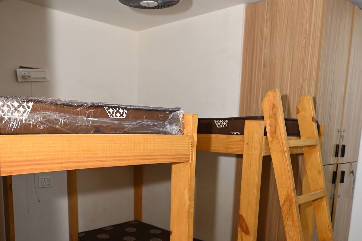 A bunk bed with a ladder, a ceiling fan, and a wardrobe in a room with white walls and tiled flooring.