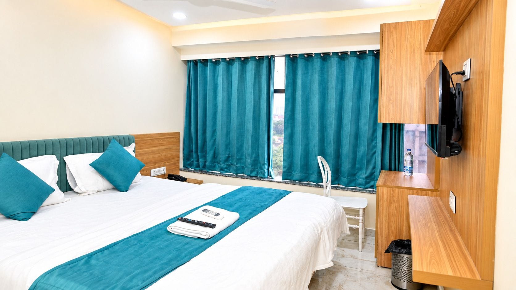 A hotel room with a bed, a desk, a chair, a TV, and a window with curtains.
