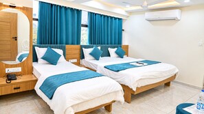 A hotel room with two beds, a wooden wardrobe, a mirror, and an air conditioning unit. - Hotel Daily Stay (Gandhinagar)