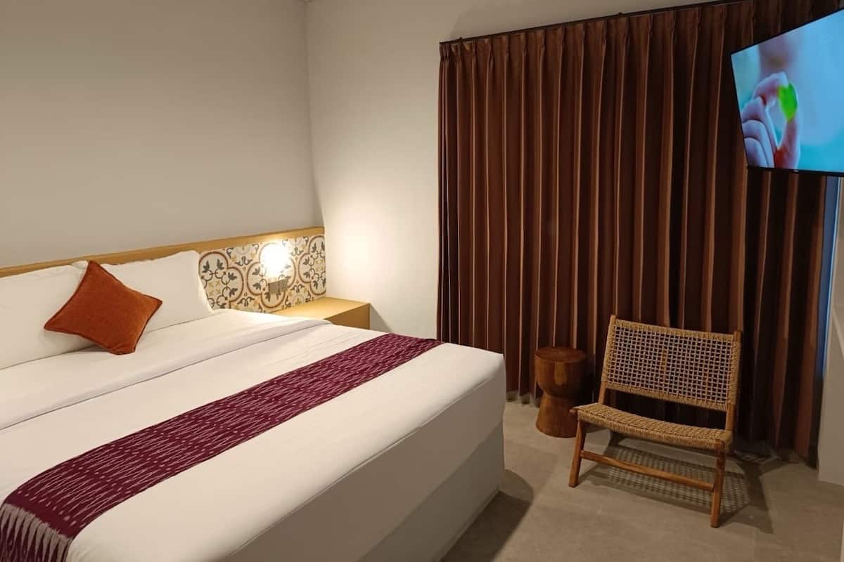 A hotel room with a large bed, a television, a wicker chair, and a curtain.