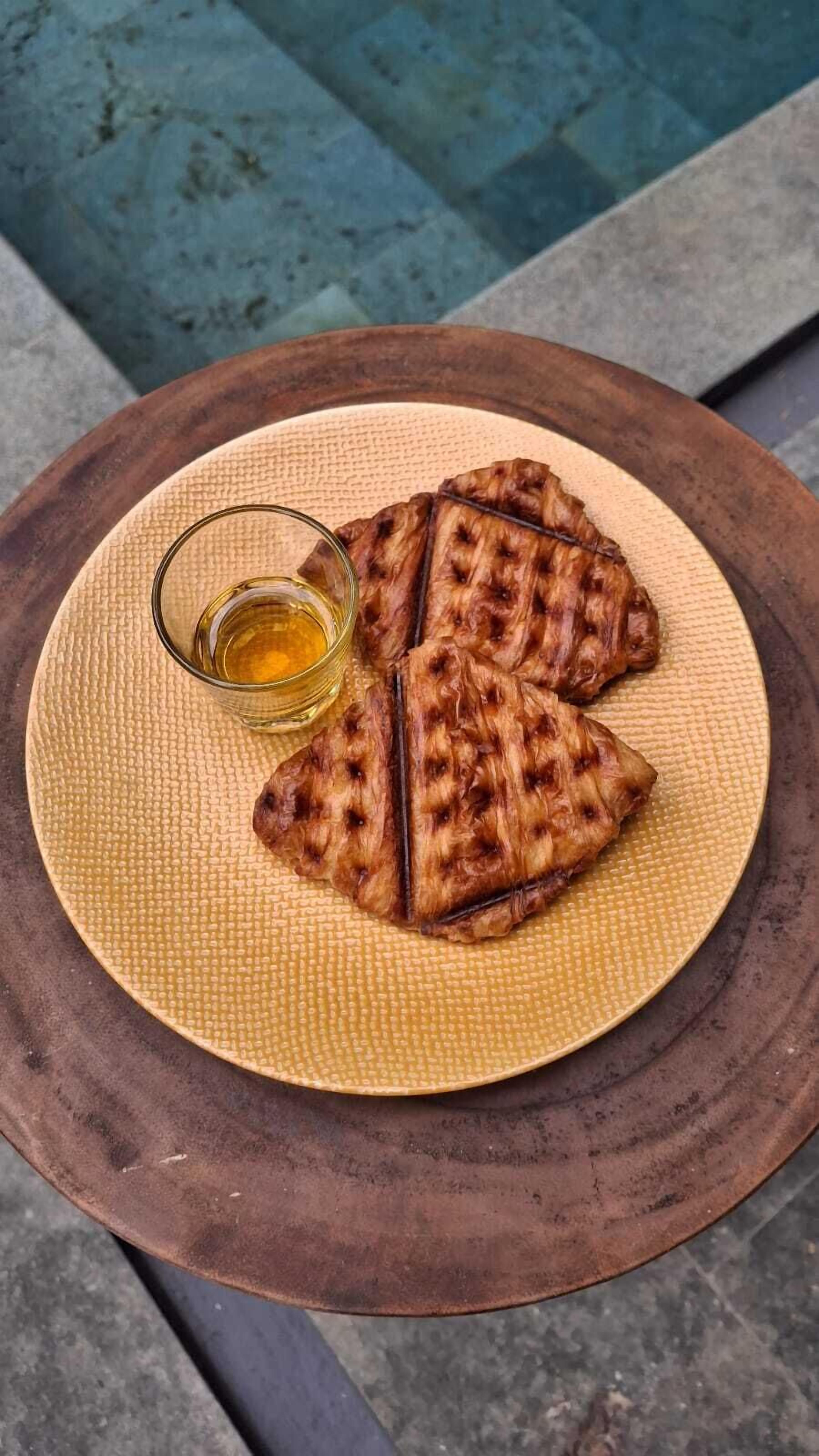 A plate of grilled sandwiches on a woven mat with a glass of oil.