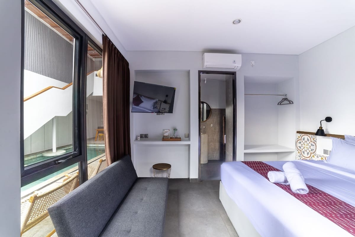 A hotel room with a bed, a sofa, a TV, a bathroom, and a view of the outside.
