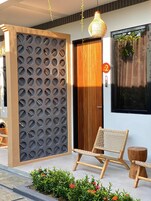 Una entrada moderna con puerta de madera, un revestimiento decorativo con círculos y una silla de mimbre junto a una pequeña mesa de madera.