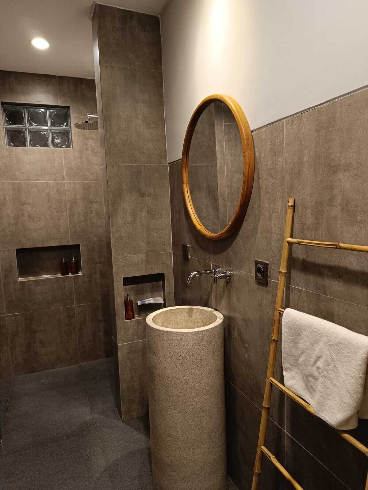 A modern bathroom with a round wooden mirror, a freestanding sink, and a towel rack.