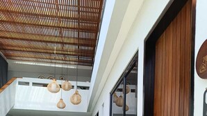 A modern indoor pool area with a wooden ceiling, wicker lounge chairs, and a dining area with a patterned backsplash. - Padinis Villa & Coffee (Sukawati)