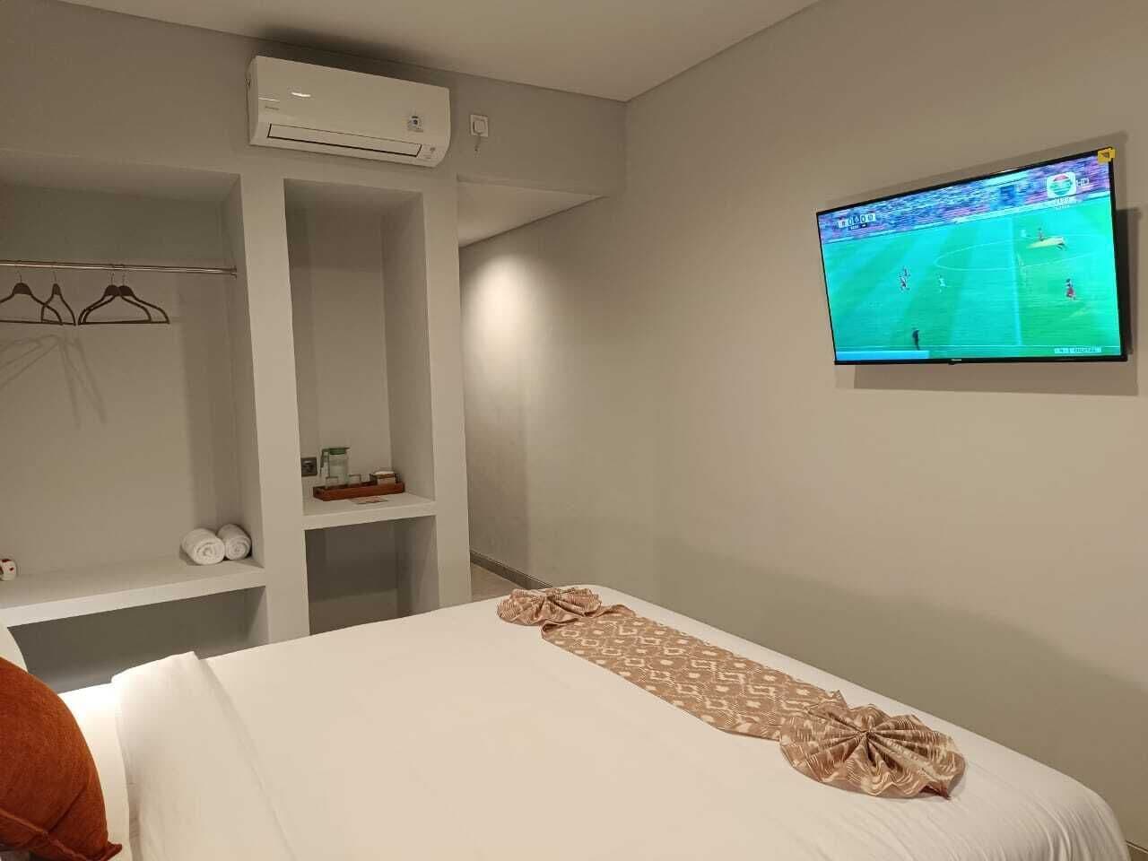 A hotel room with a bed, a TV on the wall, a wardrobe, and a shelf with toiletries.