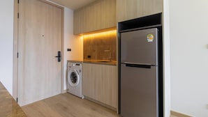 A compact kitchen with a washing machine, a refrigerator, and wooden cabinetry. - New Condo Near Beach Prime Location C228 (Choeng Thale)